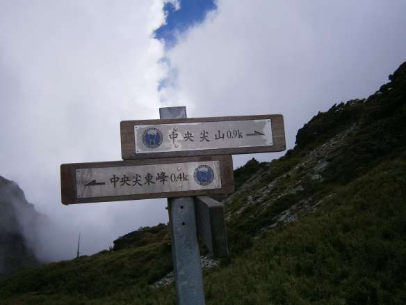A signpost marks the saddle at the top of the scree slope.